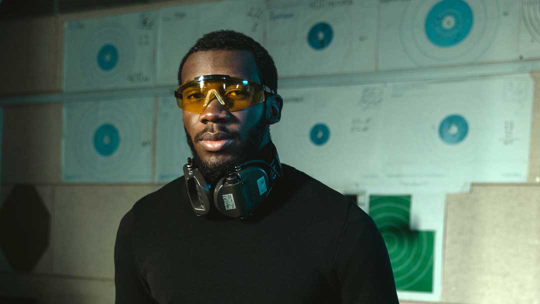 Photo of a guy with safety glasses and ear protection standing near a shooting range